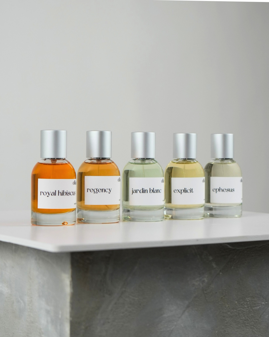 Five perfume bottles with labels on a white shelf against a gray background