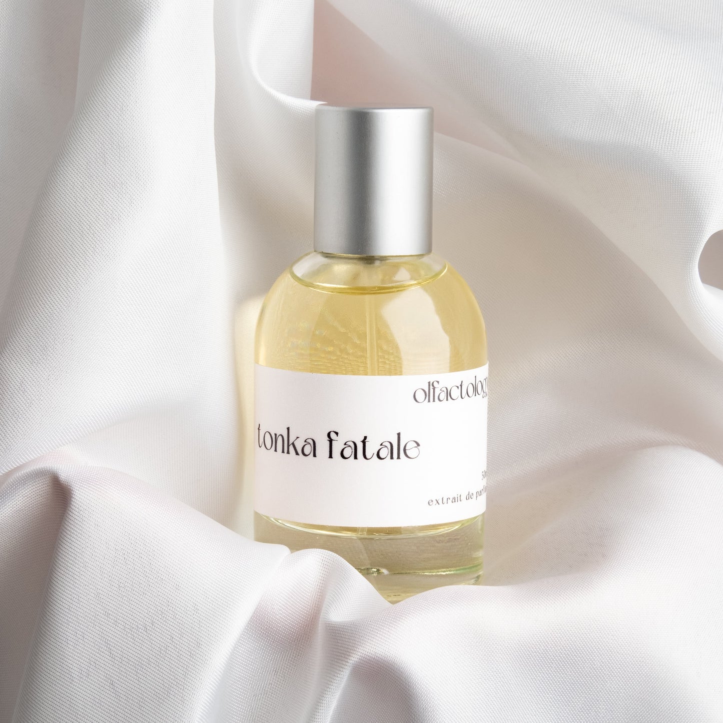 Perfume bottle labeled 'tonka fatale' on a white fabric background